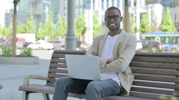 istock African Man with Laptop Smiling at Camera while Sitting Outdoor on Bench 1423641955