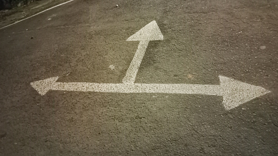 A three way arrow symbol on a black asphalt road surface.