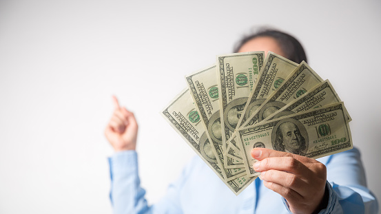 Close up woman holding dollars happy pointing with hand and finger to the side successful, showing money and boasting lottery winning, big profit. indoor studio shot isolated on gray background