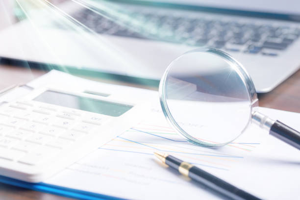 istock magnifying glass with business document financial paper chart statistic report on desk in office, closeup calculating machine with paperwork on table concept for analysis, market, banking 1423643834