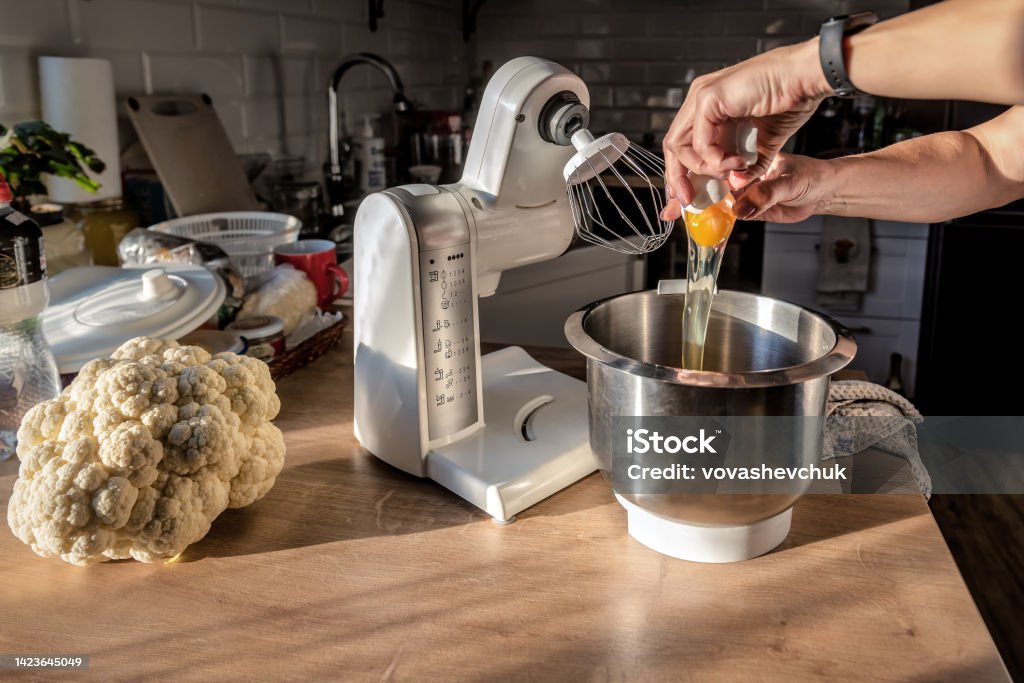Breaks an egg into the bowl of a multifunctional food processor and prepares the dough Breaks an egg into the bowl of a multifunctional food processor and prepares the dough. Cauliflower head Appliance Stock Photo