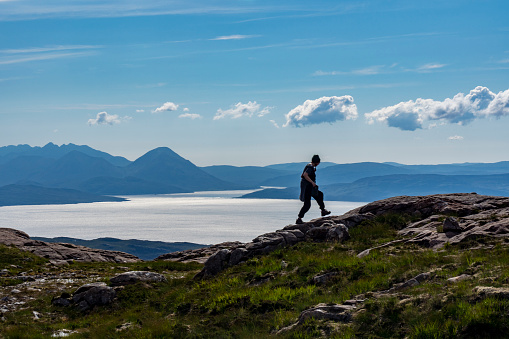 woman walking at pass of the cattle with isle of  skye in background, applecross, scotland, uk