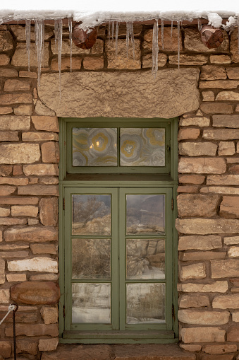 Green Window With Decorative Glass In Stone Wall With Icicles during winter