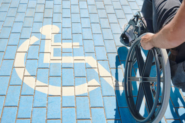 hombre discapacitado irreconocible en silla de ruedas que pasa por encima de un letrero de discapacitados pintado en el suelo - accesibilidad fotografías e imágenes de stock