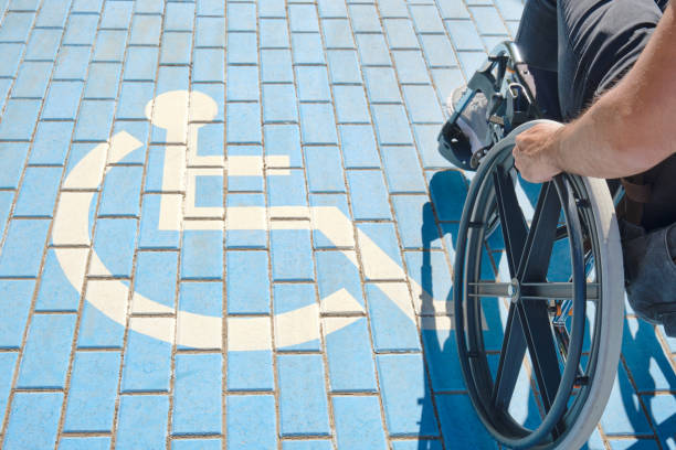 uomo handicappato irriconoscibile su una sedia a rotelle che passa sopra il cartello handicappato dipinto a terra - accessibility sign disabled sign symbol foto e immagini stock