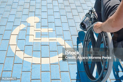 istock unrecognizable handicapped man in a wheelchair passing over handicapped sign painted on the ground 1423649571