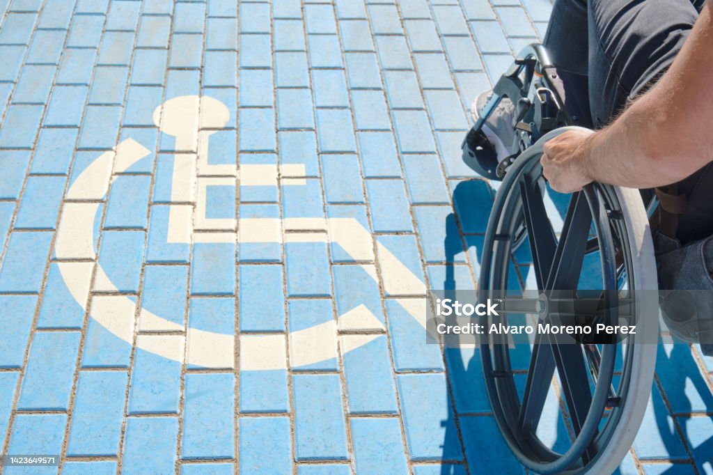 unrecognizable handicapped man in a wheelchair passing over handicapped sign painted on the ground unrecognizable handicapped man in a wheelchair passing over blue and white handicapped sign painted on the floor International Symbol Of Access Stock Photo