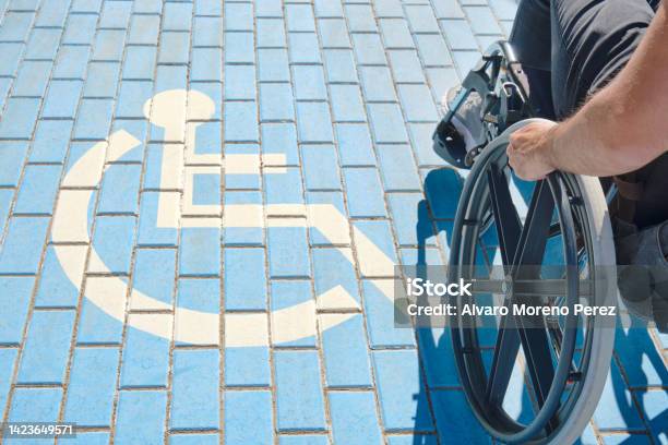 Unrecognizable Handicapped Man In A Wheelchair Passing Over Handicapped Sign Painted On The Ground Stock Photo - Download Image Now