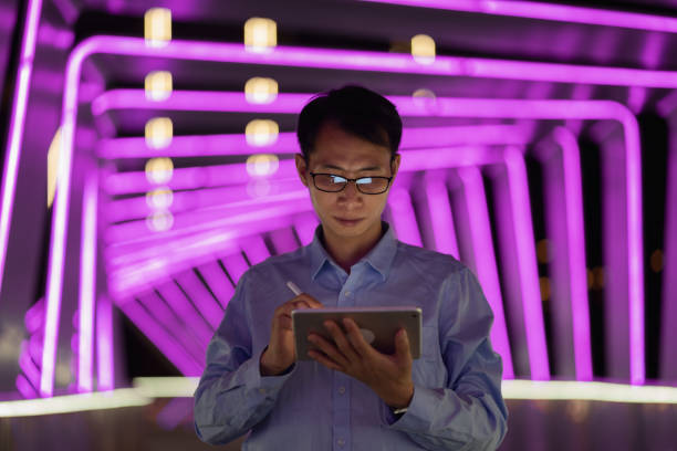 istock Man holding digital pen and using tablet on purple neon light background 1423653029