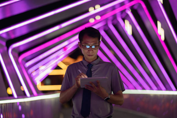 istock Man holding digital pen and using tablet on purple neon light background 1423653036
