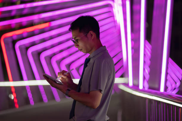 uomo che tiene la penna digitale e usa la tavoletta su sfondo viola al neon - digital tablet digitized pen touchpad men foto e immagini stock