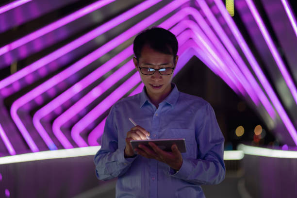 istock Man holding digital pen and using tablet on purple neon light background 1423653361