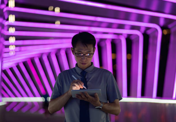 istock Man holding digital pen and using tablet on purple neon light background 1423653371