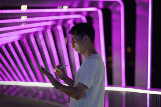 istock Man holding digital pen and using tablet on purple neon light background 1423653545