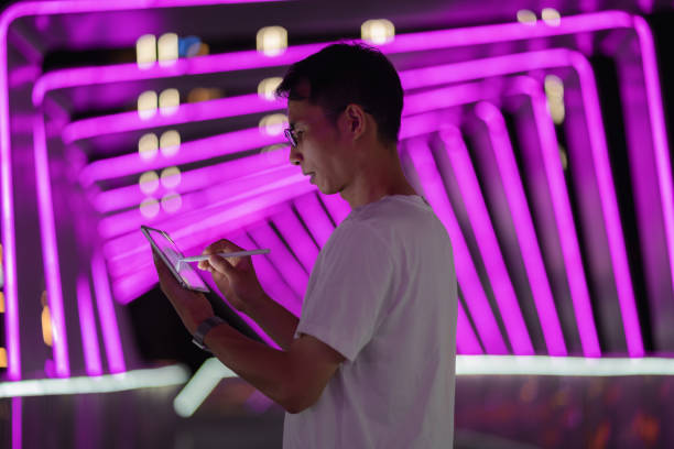 istock Man holding digital pen and using tablet on purple neon light background 1423653556