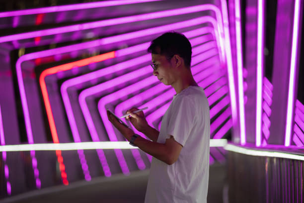 istock Man holding digital pen and using tablet on purple neon light background 1423653606