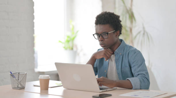 istock Young African Man Thinking while Working on Laptop in Office 1423658523