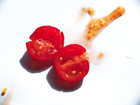 Sliced ripe tomato squashed on a white surface.