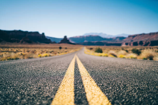 From below of long empty asphalt road with double solid running through dry desert valley in sunny cloudless day in USA