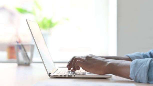 istock Side View of Young African Man Typing on Laptop Keyboard 1423663720