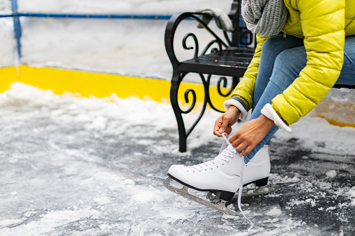 Young African woman tying shoelace on ice skate