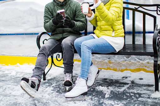 Young adult couple resting at ice skate ring and drinking coffee