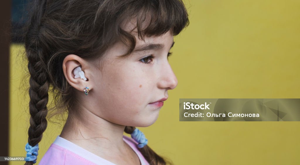 Girl with a warming therapeutic cotton swab in the ear with a sad and tearful face is holding her ear. Ear pain, otitis media, swelling of cheek, gums, toothache, children's surgery, otolaryngology Earache Stock Photo