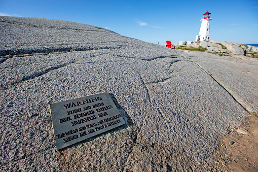 Landmark lighthouse at Peggy's Cove, Nova Scotia on a summer morning with blue skies. A danger sign in the foreground