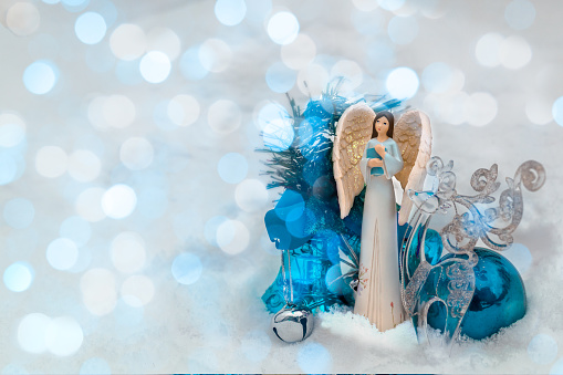 A Christmas guardian angel in blue clothes with a book in the snow with blue balloons and a glass deer. christmas decoration. A fabulous postcard. Space for text.
