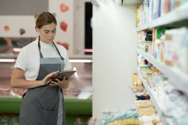 istock Female sales clerk wearing apron using a digital tablet with store shelves on background. 1423674448