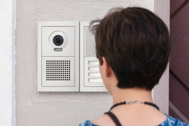 A person using a door entry phone with a camera at a building entrance.