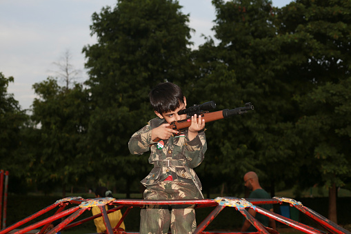 Little soldier of Indian ethnicity shooting with rifle outdoor in nature portrait close up.