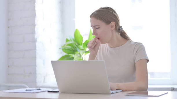 istock Woman Coughing while Working on Laptop 1423684768