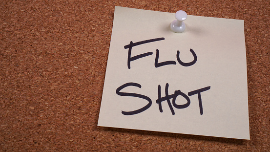 Sticky note reminder to get a flu shot posted on a cork bulletin board