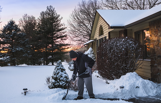 Senior man shoveling his driveway after snowfall in Midwest
