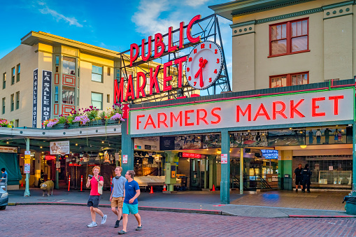 People cross street in front of the landmark Pike Place Market in downtown Seattle, Washington, USA at sunset.