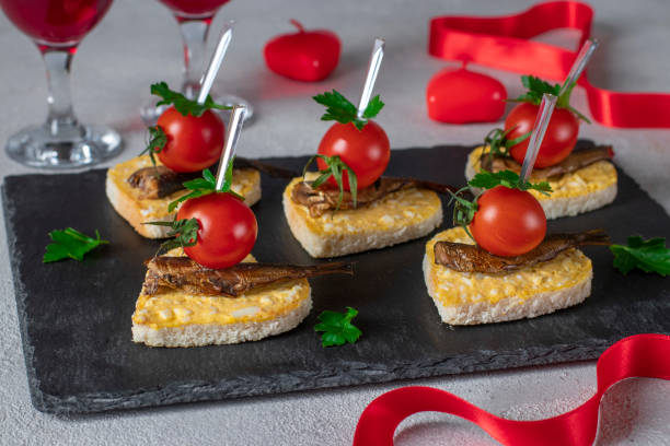 canape in the form of hearts with sprats, cheese, egg and cherry tomatoes on slate plate on light gray background, idea for valentine's day - cherry valentine stok fotoğraflar ve resimler