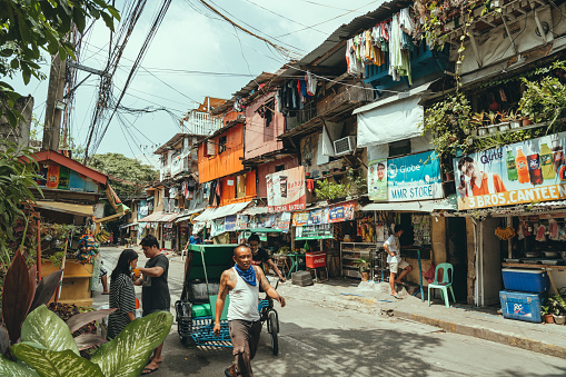 Manila, Philippines - March 05, 2022: Slums and illegal settlements scattered across the metropolitan area in downtown near the street. People do daily work and walk around.