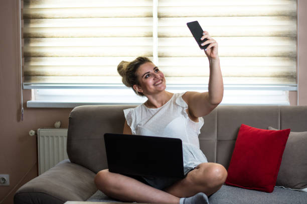 istock Smiling young  woman taking selfies and using a laptop at home 1423703643