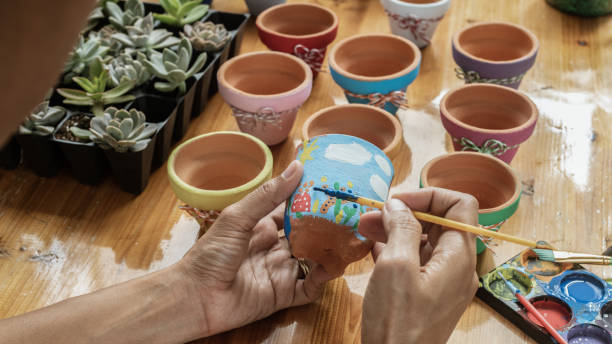 Hands of a Latin mixed raced woman, painting clay pots to plant succulent plants Hands of a Latin mixed raced woman, painting clay pots to plant succulent plants on a wooden table with natural lighting and acrylic paints painted flower pots stock pictures, royalty-free photos & images