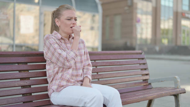 istock Young Woman Coughing while Sitting on Bench Outdoor 1423709406