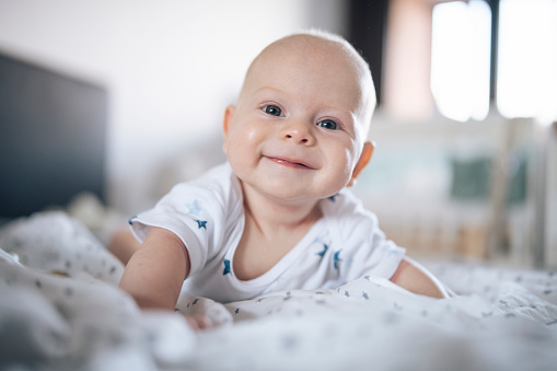 Portrait of smiling, joyful baby boy laying on front and looking at the camera.