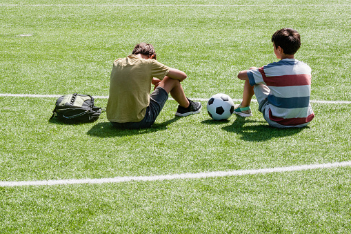 Children talking in school stadium outdoors. Teenage boy comforting consoling upset sad friend. Education, bullying, conflict, social relations, problems at school, learning difficulties concept.