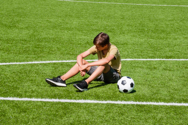 Sad alone teenage boy sitting in empty school sport stadium outdoors. Emotions, defeat, lost game, difficulties, problems of teenagers stock photo