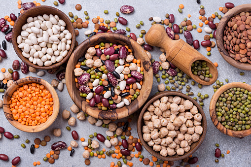 Top view of different beans, lentils, mung, chickpeas in wooden bowls for tasty meals on grey concrete background
