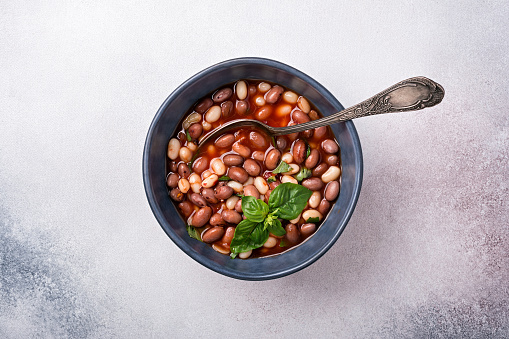 Top view of spicy dish with beans in tomato sauce with fresh basil on grey concrete background