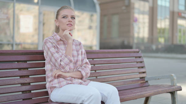 istock Pensive Young Woman Thinking while Sitting Outdoor on Bench 1423728395