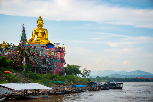 Golden Seated Buddha in a Boat on the Shore of the Mekong at Phra Chiang Saen Si Phaendin Temple. Laos and Myanmar in the background