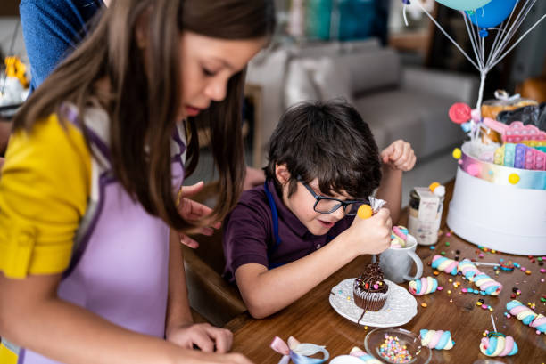 hermanos abriendo y jugando con dulces en un día de niños en casa - baked cake cupcake decoration fotografías e imágenes de stock