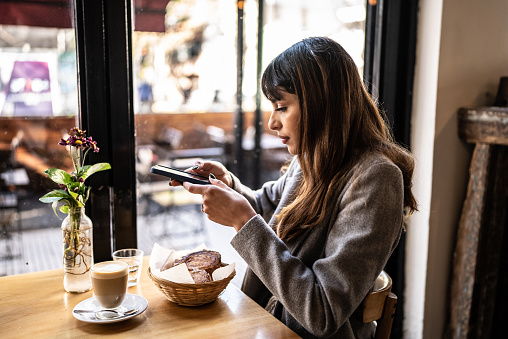 Young woman taking a photo of the toasted bread and cappuccino at coffee shop